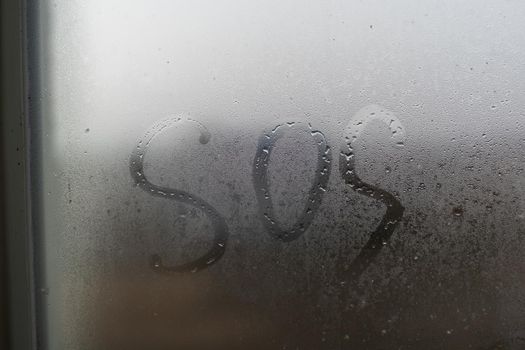 close-up inscription word SOS on a foggy window.