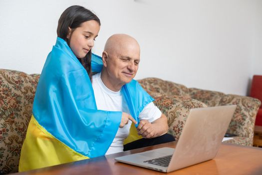 Grandfather and granddaughter with laptop and flag of Ukraine.