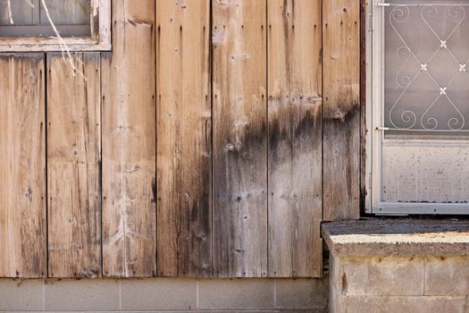 Close up of Weathered Wood Siding In State of Neglect and Disrepair Beginning Moldy Weathered and Rotting Around Front Step of Cottage or House. Copy Space Left