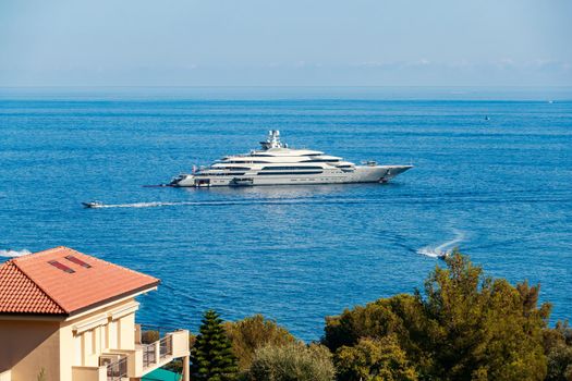 The huge mega yacht is moored in sea off the coast of the azur coastline at sunny day, the chrome plated handrail, sun reflection on glossy board of the motor boat. High quality photo