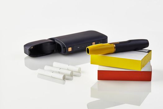 New generation black electronic cigarette is on packs with red and yellow sides, open battery, three heatsticks isolated on white. Heating tobacco system. Template place for your text, image. Close up