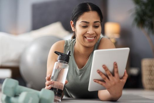 Shot of a sporty young woman using a digital tablet while exercising at home.