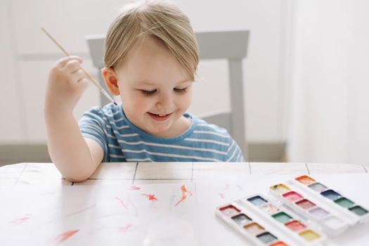 Child painting and drawing with watercolor paint at white table. Development of creative potential in children