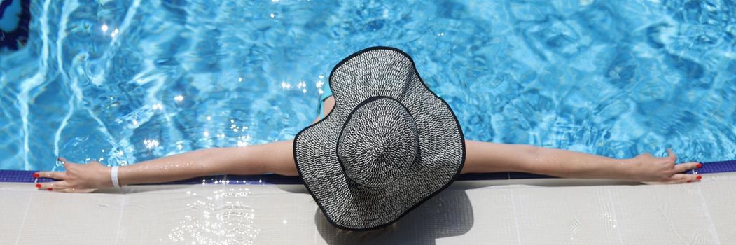 Woman in panama lying on edge of swimming pool top view. Relaxation at resort concept