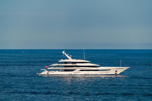 The huge mega yacht is moored in sea off the coast of the azur coastline at sunny day, the chrome plated handrail, sun reflection on glossy board of the motor boat. High quality photo