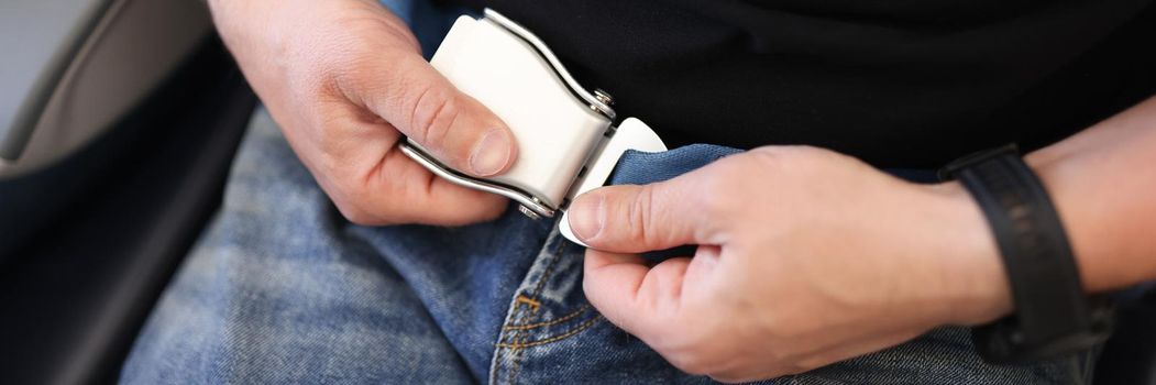 Male hands fastening seat belt in aircraft cabin closeup. Air travel safety concept