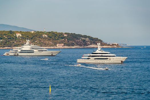 The two huge mega yachts are moored in sea at sunny day, the chrome plated handrail, sun reflection on glossy board of the motor boat. High quality photo