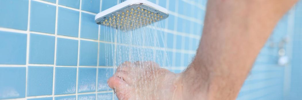 Man washing his feet from sand under shower on beach closeup. Foot hygiene concept