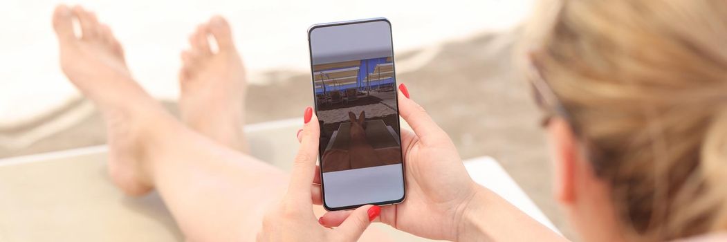 Young woman lying on sun lounger on beach and taking pictures of her feet on mobile phone closeup. Photo on social networks concept