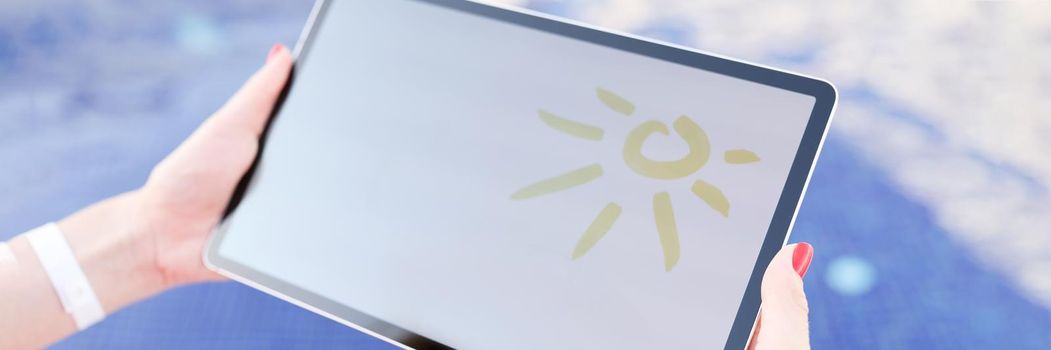 Female hands holding digital tablet with drawn sun over pool closeup. Online weather forecast concept