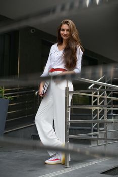 Beautiful young caucasian businesswoman in a white clothes with a laptop and notebook outdoor near business centre.