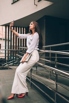 Beautiful young caucasian businesswoman in a white clothes with a laptop and notebook outdoor near business centre.