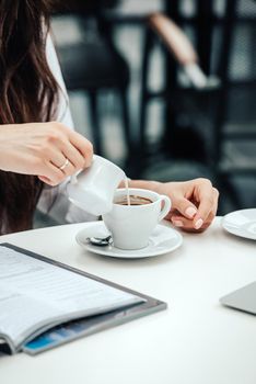 woman in a cafe pours milk cream into coffee cup. businesswoman lifestyle background