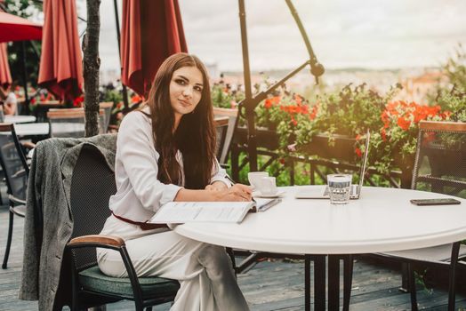 Smiling young dark-haired businesswoman makes notes in a notebook in a cafe on a summer day. Business, e-learning, freelance concept. laptop on a table.