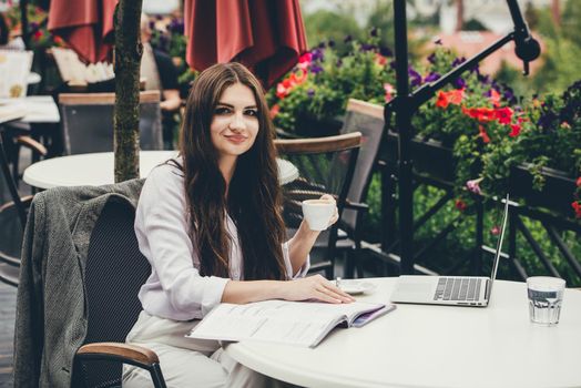 Young brunette woman using laptop computer sitting at cafe table and drik coffe. . Business People Concept