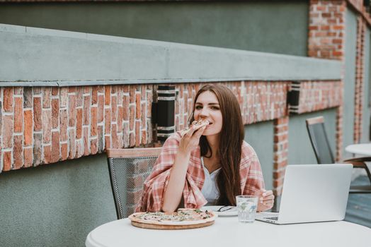 Young freelancer woman using laptop computer and eat pizza while sitting at cafe table. Business People Concept