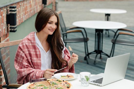 Young freelancer woman using laptop computer and eat pizza while sitting at cafe table. Business People Concept