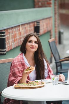 Young freelancer woman using laptop computer and eat pizza while sitting at cafe table. Business People Concept