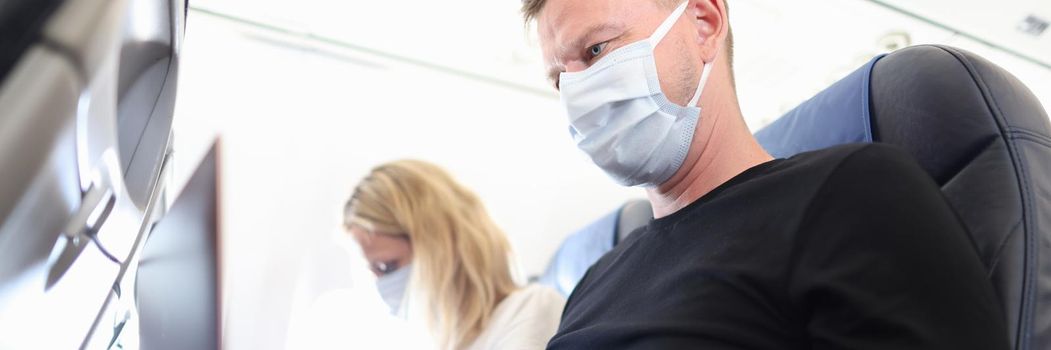 Man and woman in protective masks working on laptops in aircraft cabin. Teleworking during covid19 pandemic concept