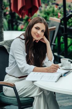 Smiling young dark-haired businesswoman makes notes in a notebook in a cafe on a summer day. Business, e-learning, freelance concept. laptop on a table.
