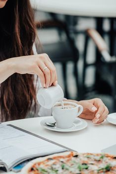 woman in a cafe pours milk cream into coffee cup. businesswoman lifestyle background