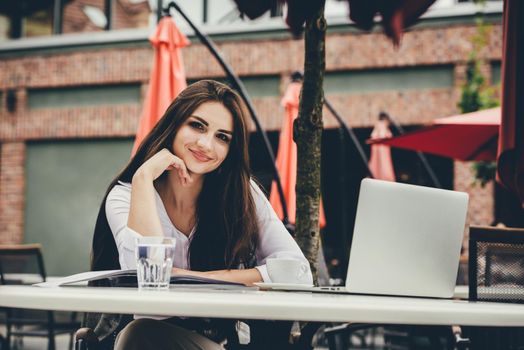 Young brunette woman using laptop computer sitting at cafe table and drik coffe. . Business People Concept