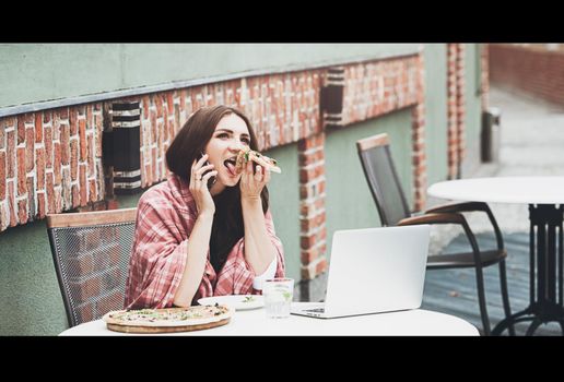 Young freelancer woman using laptop computer and eat pizza while sitting at cafe table. Business People Concept