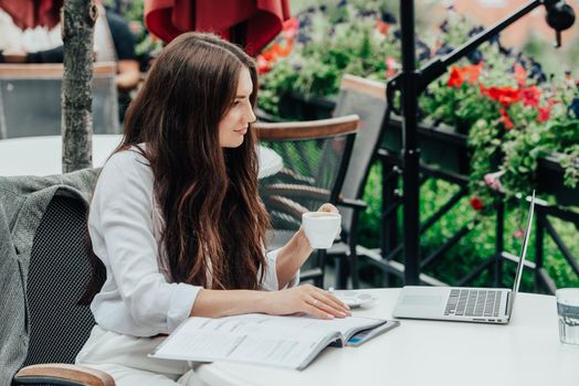 Young brunette woman using laptop computer sitting at cafe table and drik coffe. . Business People Concept