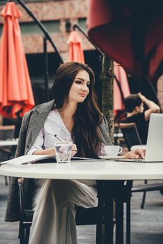 Young brunette woman using laptop computer sitting at cafe table and drik coffe. . Business People Concept