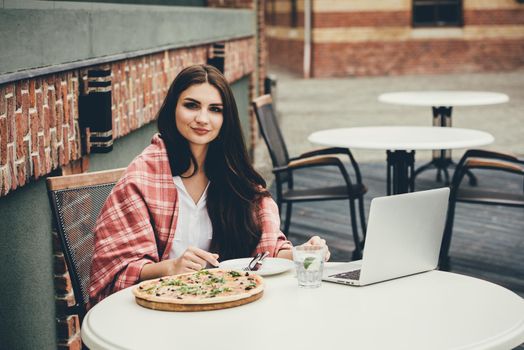 Young freelancer woman using laptop computer and eat pizza while sitting at cafe table. Business People Concept