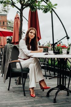 Smiling young dark-haired businesswoman makes notes in a notebook in a cafe on a summer day. Business, e-learning, freelance concept. laptop on a table.