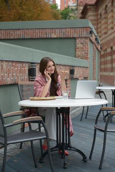 Young freelancer woman using laptop computer and eat pizza while sitting at cafe table. Business People Concept