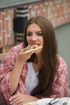 Beautiful brunette girl in a white blouse eating pizza at restaurant. Outdoors