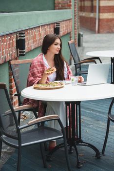 Young freelancer woman using laptop computer and eat pizza while sitting at cafe table. Business People Concept