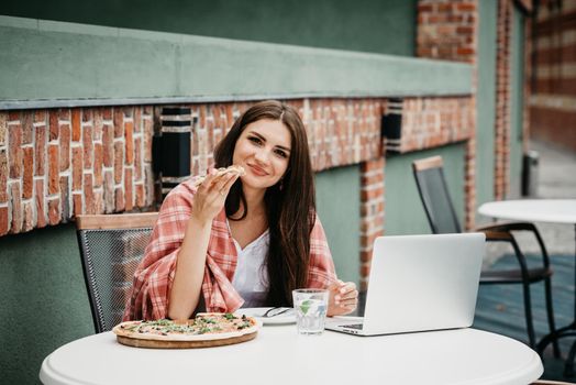 Young freelancer woman using laptop computer and eat pizza while sitting at cafe table. Business People Concept