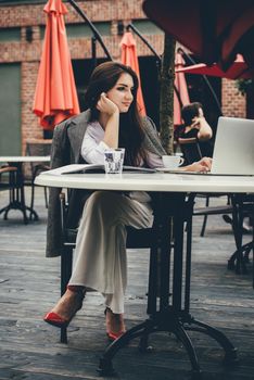 Young brunette woman using laptop computer sitting at cafe table and drik coffe. . Business People Concept