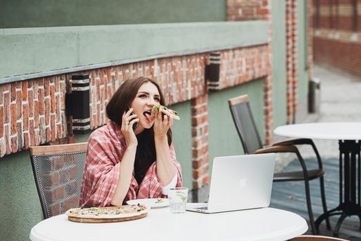 Young freelancer woman using laptop computer and eat pizza while sitting at cafe table. Business People Concept