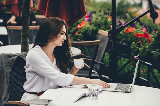 Young brunette woman using laptop computer sitting at cafe table and drik coffe. . Business People Concept