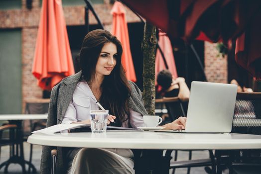 Young brunette woman using laptop computer sitting at cafe table and drik coffe. . Business People Concept