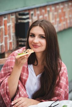 Beautiful brunette girl in a white blouse eating pizza at restaurant. Outdoors