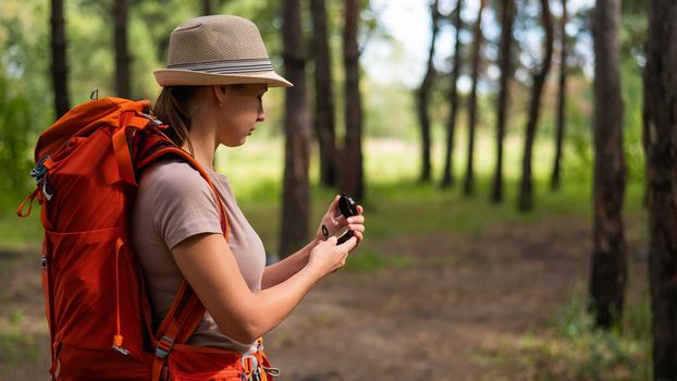 Young caucasian woman is hiking and using a compass in the forest