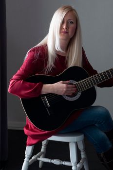 beautiful young blonde woman in a red dress with a black guitar, favorite hobby, music project. High quality photo