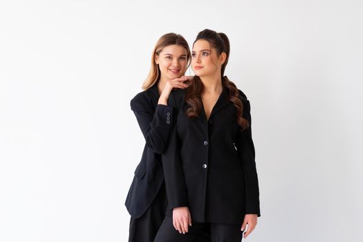 Concept of partnership in business. Two Young businesswoman dressed black formal suit standing studio isolated white background.Blonde woman put her hands on the shoulders of her friend. Smile