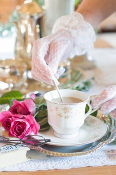 English retro still life and a woman's hand in a white lace glove stirring coffee with milk in an elegant cup from Chinese porcelain, light and airy early morning mood. High quality photo