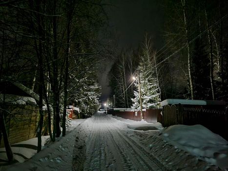 Russian village at night in winter. A road covered with snow and light from the windows of houses