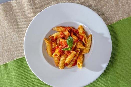 Serving of spicy savory italian penne pasta garnished with fresh basil and topped with grated Parmigiano-Reggiano, or parmesan, cheese