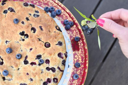 a woman's hand decorates a fresh pie with blueberries, bucking at home, exotic food, delicious dessert. High quality photo