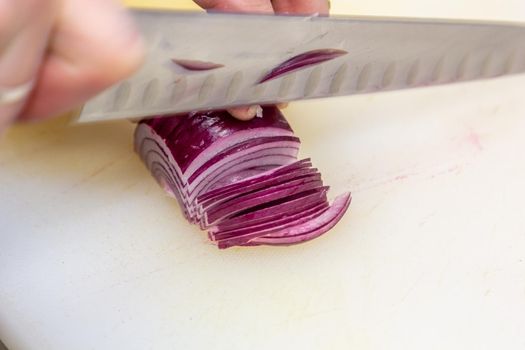 Chef choppig a red onion with a knife on the cutting board, chef at work.