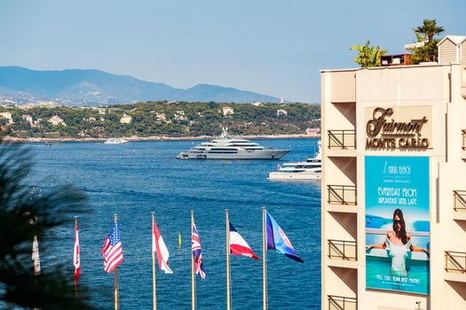 Monaco, Monte Carlo, 21 August 2017: The hotel Fairmont, flags of different countries on flagpoles, mega yachts on background, Mediterranean Sea and island. High quality photo
