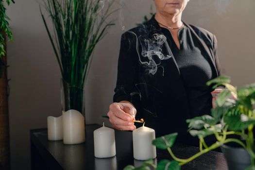 Portrait of a blonde-haired, mature, concentrated and professional beautician woman lighting scented candles to start a treatment in her spa business. Relaxing atmosphere and dim lighting, decoration of plants and candles, massage table in background and towels. Horizontal. cropped plan